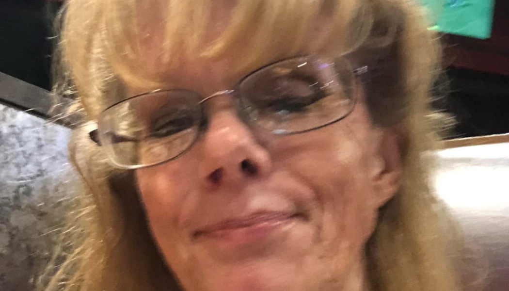 Close-up portrait of a smiling woman with blonde hair and glasses.