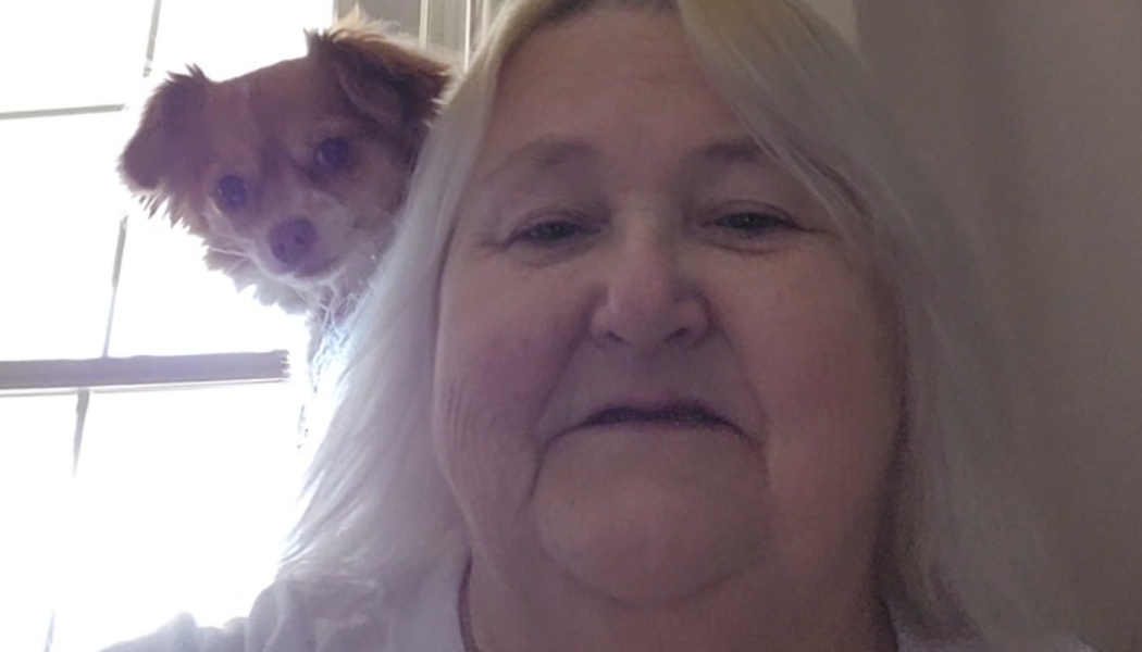 Close-up selfie of a woman with long white hair and a small brown dog peeking over her shoulder.