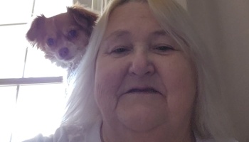 Close-up selfie of a woman with long white hair and a small brown dog peeking over her shoulder.