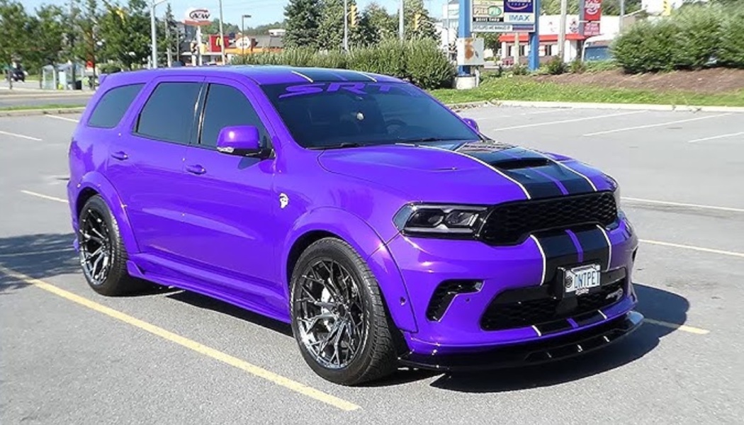 Bright purple Dodge Durango SRT SUV with black racing stripes parked in an open parking lot.
