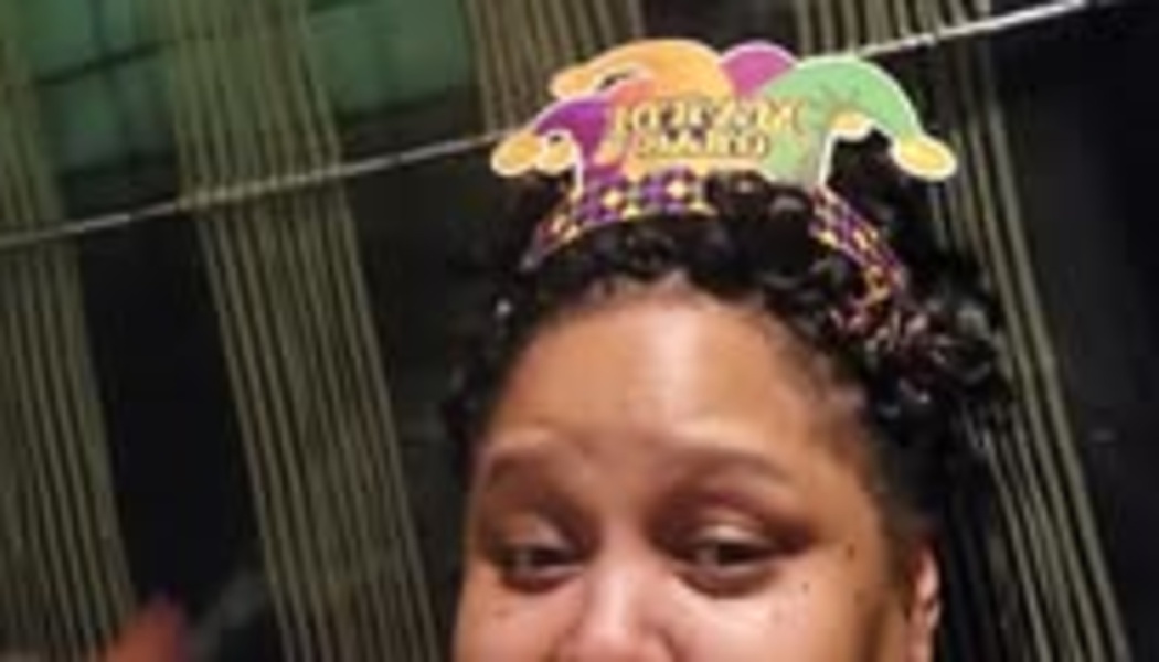 A woman wearing a colorful Mardi Gras jester hat headband on top of her dark curly hair.