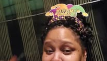 A woman wearing a colorful Mardi Gras jester hat headband on top of her dark curly hair.