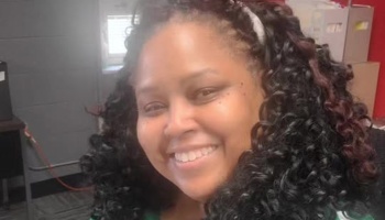 A smiling woman with long, dark curly hair looking at the camera.