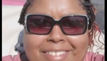 Close-up selfie of a smiling Black woman wearing dark sunglasses.