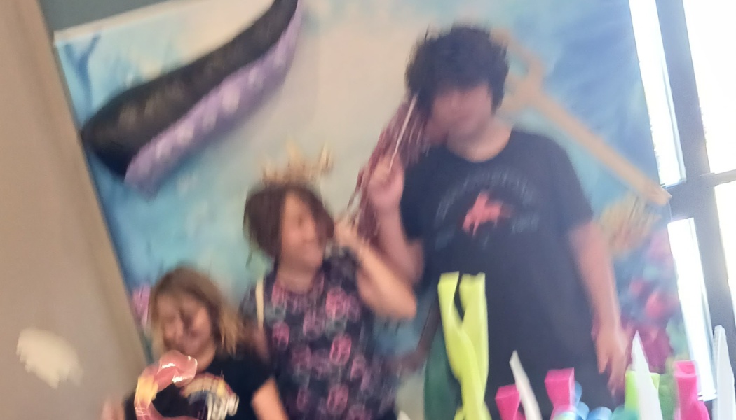 Three people posing excitedly in front of an under-the-sea mural with giant octopus tentacles and ocean props.