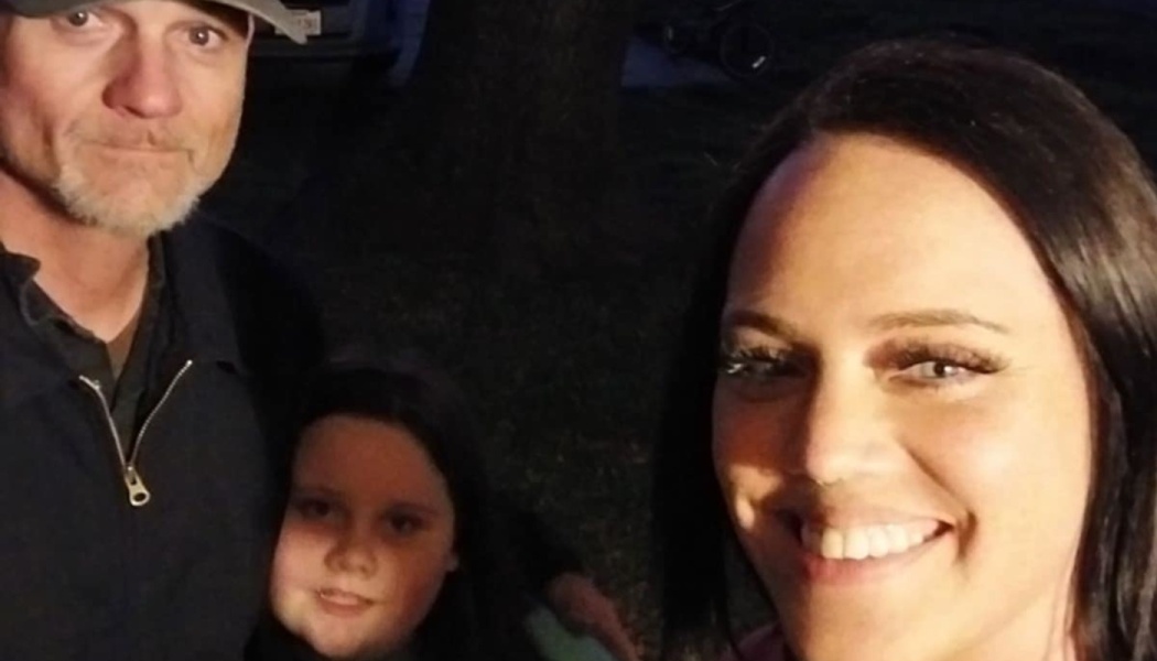A smiling woman, a man in a baseball cap, and a young girl pose together for a family selfie at night.