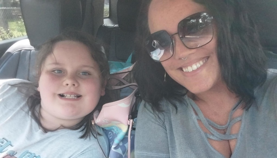 A smiling woman wearing sunglasses and a young girl taking a selfie inside a car.