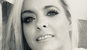 Black and white close-up portrait of a blonde woman smiling slightly at the camera.
