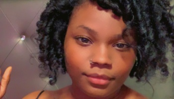 Close-up portrait of a young Black woman with curly dark hair and a nose ring looking at the camera.
