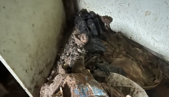 Mud-covered debris, black plastic bags, and dirty cloth piled in the corner of a water-damaged room.