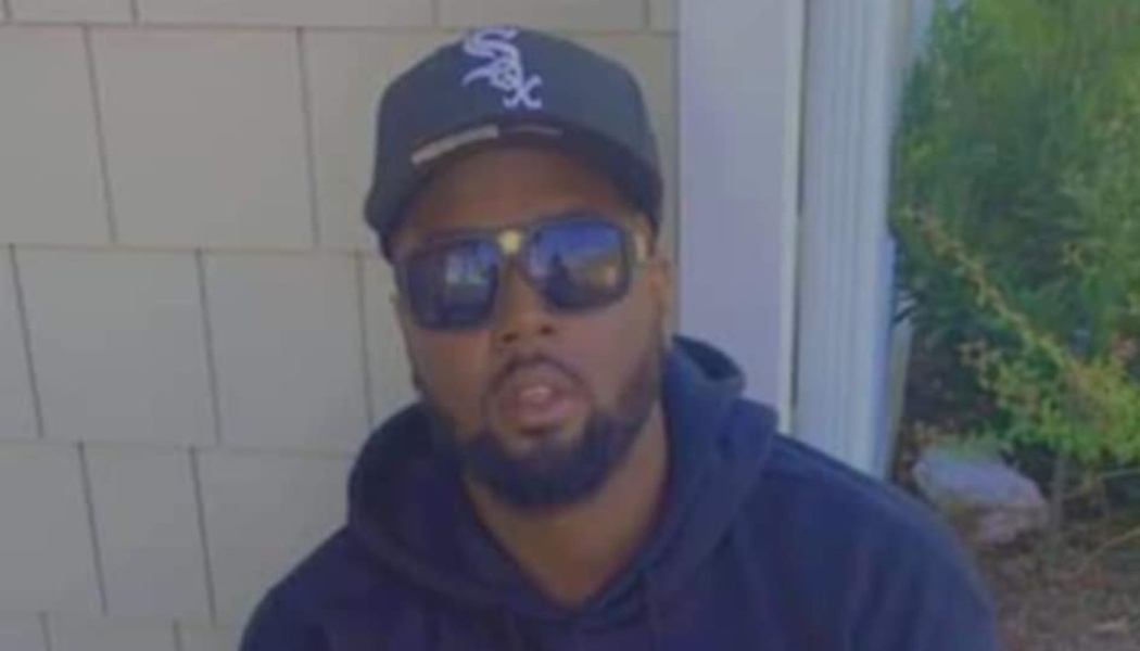 A bearded man wearing a black Chicago White Sox baseball cap, sunglasses, and a hoodie.