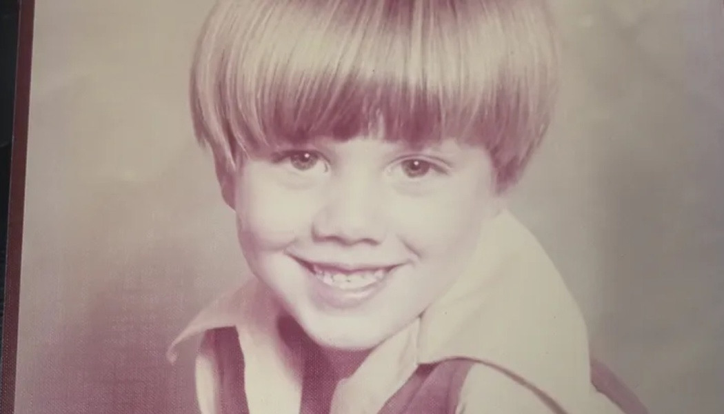 Young boy with a bowl cut smiling brightly in a vintage school portrait.