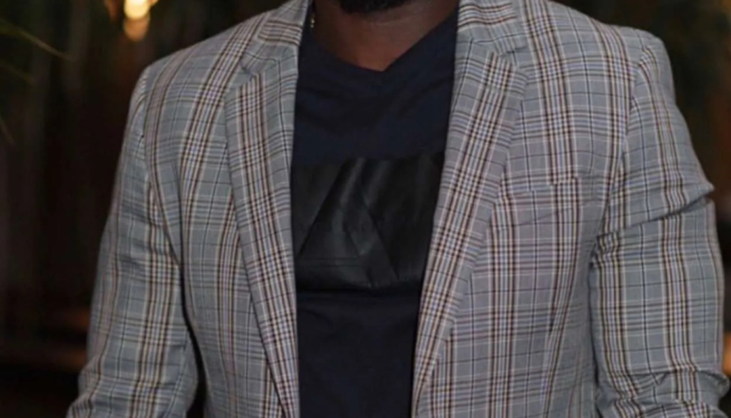 Torso of a man wearing a tailored grey plaid blazer over a dark v-neck shirt.