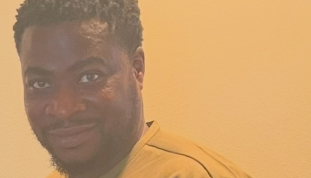 Close-up portrait of a smiling Black man with short hair wearing a yellow shirt.