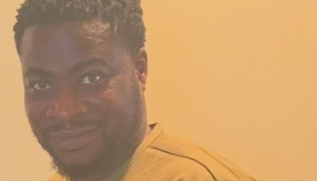 Close-up portrait of a smiling Black man with short hair wearing a yellow shirt.