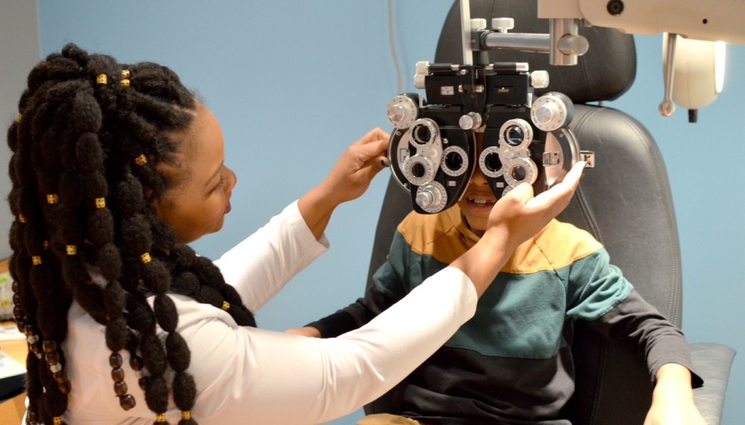 A female optometrist adjusts a phoropter during a young boy's eye exam.