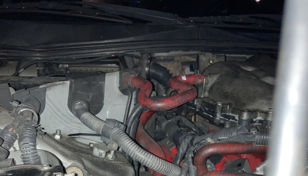 Close-up of a car engine bay showing red silicone coolant hoses, black wiring harnesses, and metal components.