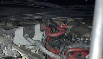 Close-up of a car engine bay showing red silicone coolant hoses, black wiring harnesses, and metal components.