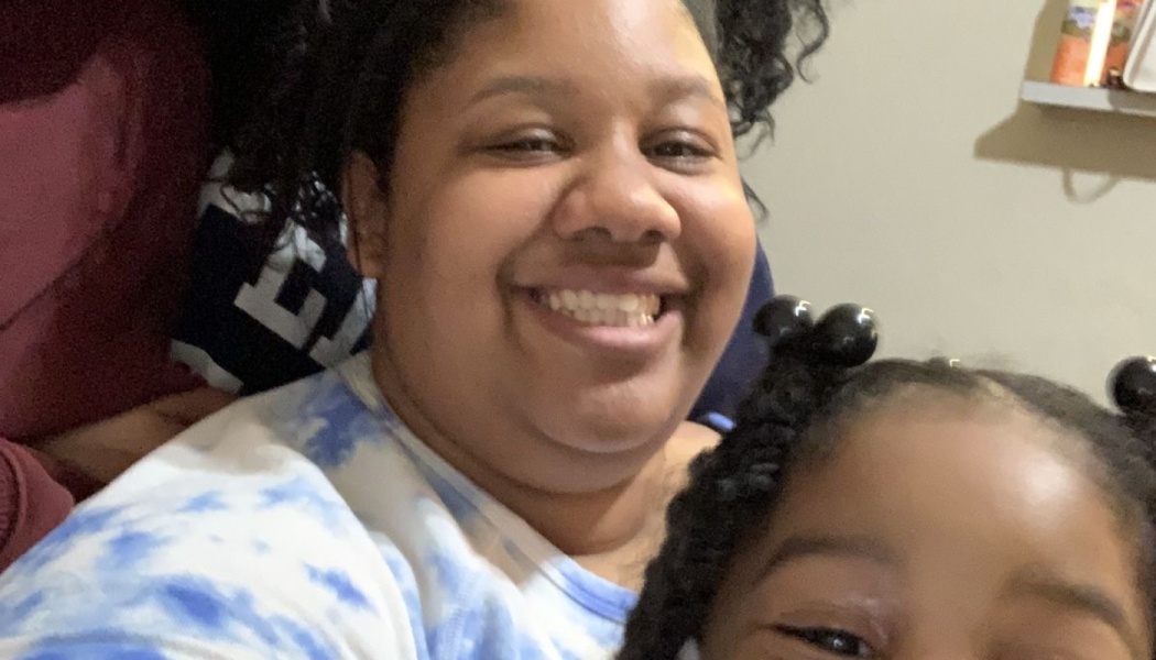 A smiling woman in a blue and white tie-dye shirt poses warmly close to a young child.