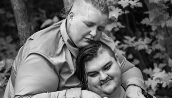 Black and white portrait of a couple sharing a tender embrace, one resting their head gently on the other.