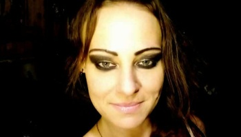 Close-up portrait of a woman with dark hair, heavy smoky eye makeup, and a slight smile.