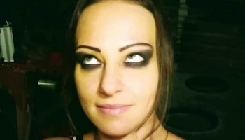 Close-up portrait of a woman with heavy dark eye makeup looking upward.