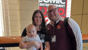 A smiling couple and their baby pose together at a comic entertainment expo.