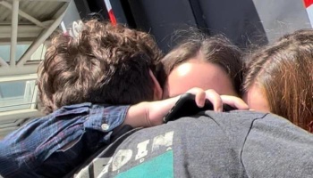 Three young people tightly embracing in a supportive group hug.