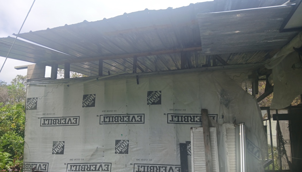 An unfinished structure with a corrugated metal roof and white weather barrier wrap covering the walls.
