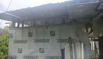 An unfinished structure with a corrugated metal roof and white weather barrier wrap covering the walls.