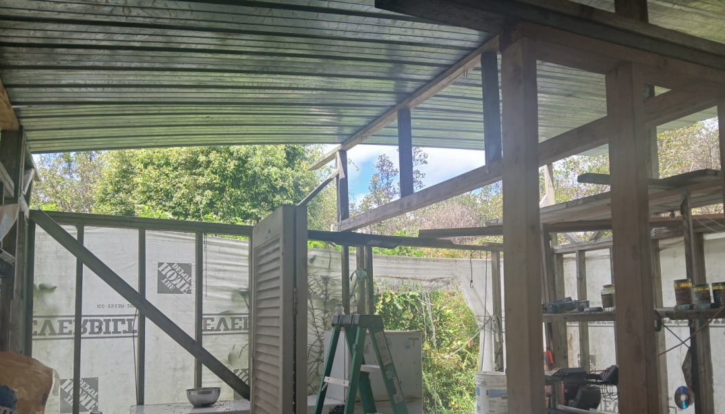 Interior of an unfinished wooden building with exposed framing studs, a stepladder, and a corrugated metal roof.