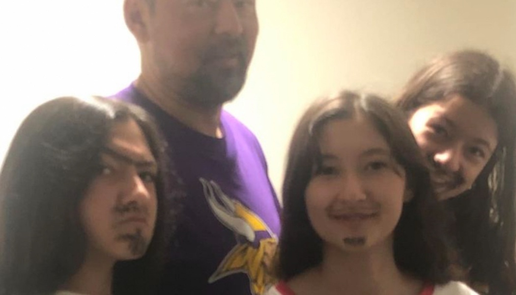 A father in a Vikings t-shirt poses with three kids who have drawn-on goatees matching his facial hair.