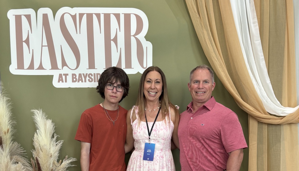 A family of three posing together in front of an Easter at Bayside event backdrop.