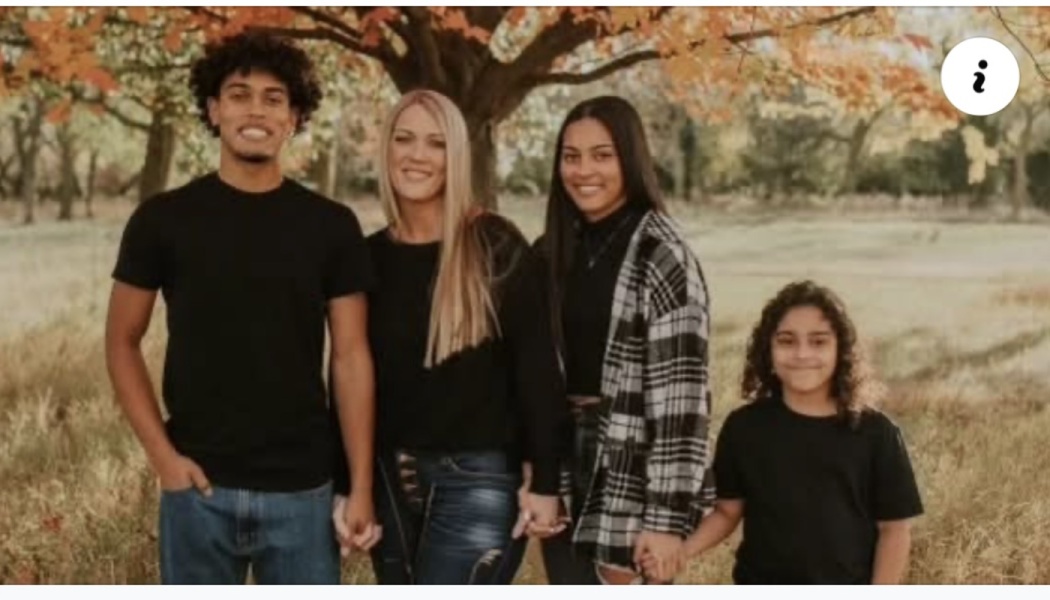 A smiling family of four standing together and holding hands in an autumn park.