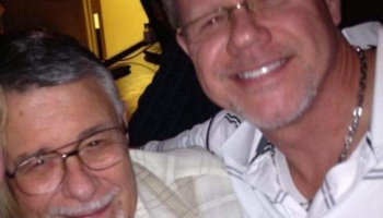 Two smiling men wearing glasses pose closely together.