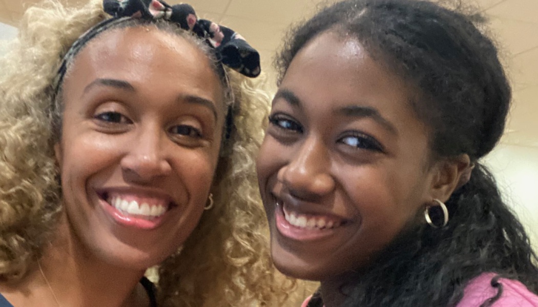 Two smiling Black women close together, one with curly blonde hair in a headband and the other with dark hair.