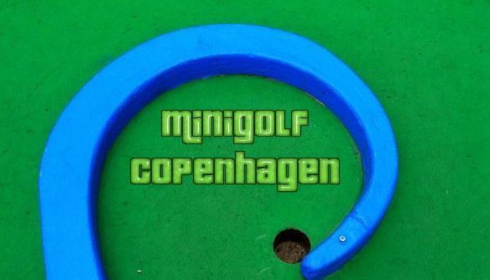 Green minigolf course with a curved blue obstacle, a hole, and text reading "Minigolf Copenhagen".