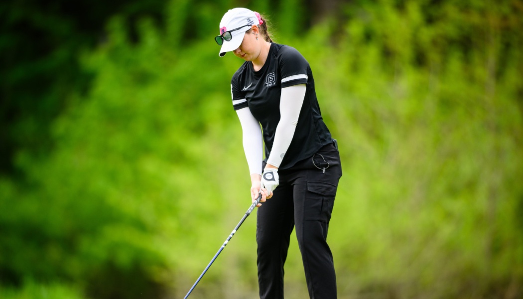 A female golfer in a white visor and black shirt lining up her shot on a green course.