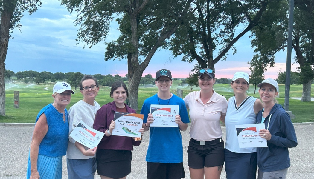 Seven golfers pose smiling on a golf course, holding personal best achievement signs.