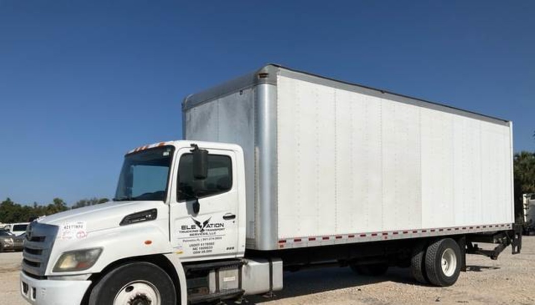 Large white commercial box truck with company logo parked under a clear blue sky.