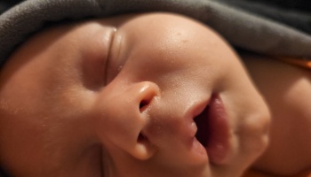Close-up of a sleeping newborn baby's face with eyes closed and mouth slightly open.
