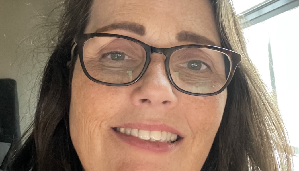 Close-up portrait of a smiling woman with dark hair wearing glasses.