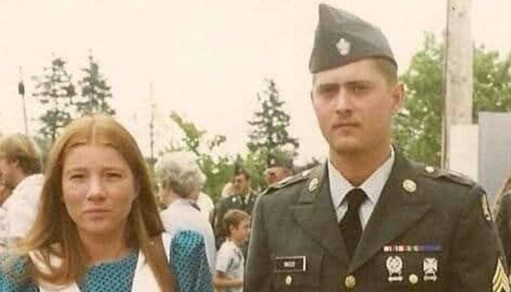A young soldier in military dress uniform stands next to a woman in a vintage portrait.