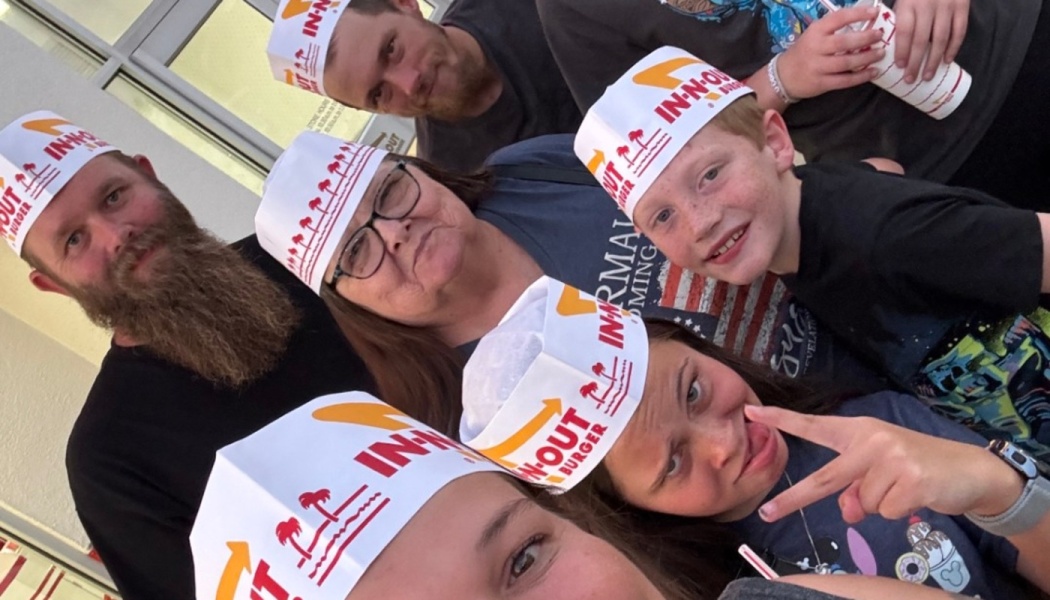 A smiling family taking a close-up group selfie while wearing paper In-N-Out Burger hats.