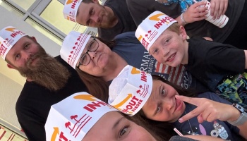A smiling family taking a close-up group selfie while wearing paper In-N-Out Burger hats.