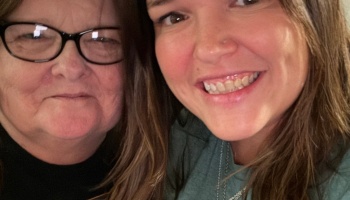 Close-up selfie of an older woman with glasses beside a younger woman smiling broadly.