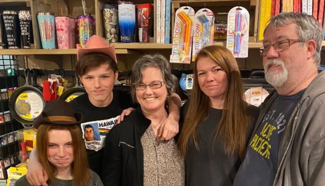 A smiling family of five poses together inside a store, with two younger members wearing fun hats.