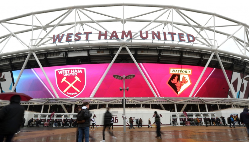 Exterior view of West Ham United stadium with a giant screen displaying West Ham and Watford club crests.