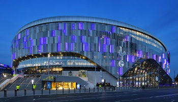 Modern Tottenham Hotspur Stadium exterior illuminated with purple lights at twilight.