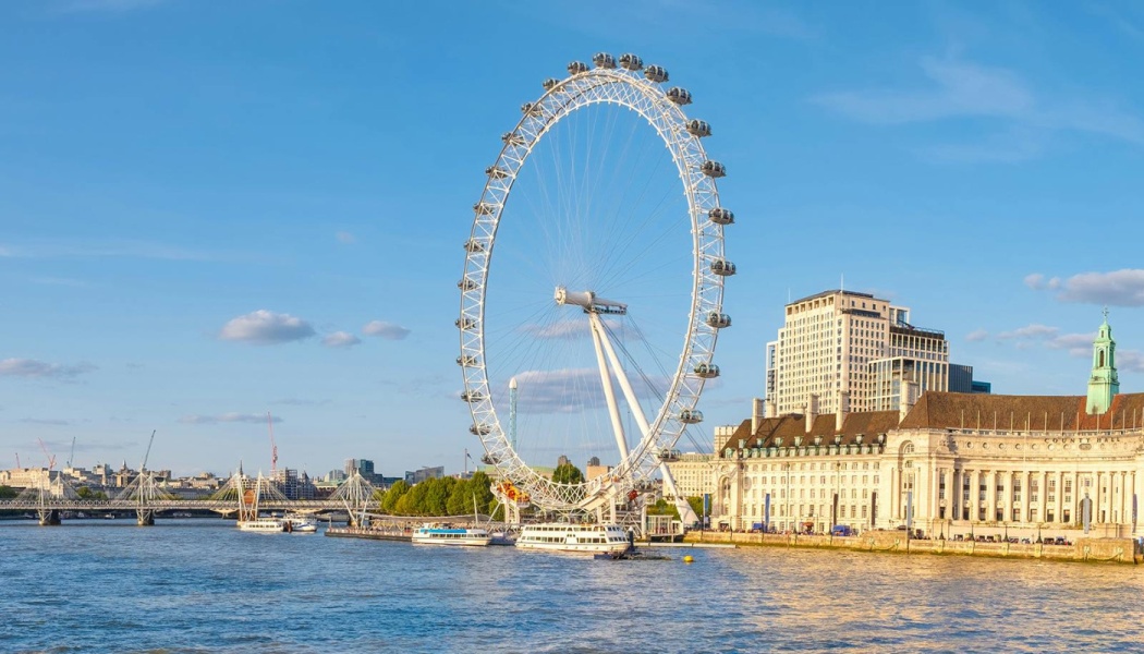 The London Eye observation wheel standing along the River Thames in London under a clear blue sky.